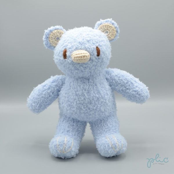 Peluche de 30cm de haut représentant un ourson bleu pâle, tricotée par Plic.